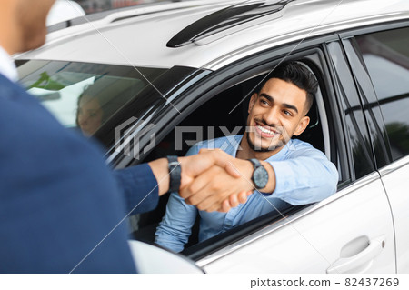 Cheerful arabic man sitting in new white car, shaking hand Cheerful arabic man sitting in new white car, shaking hand 82437269