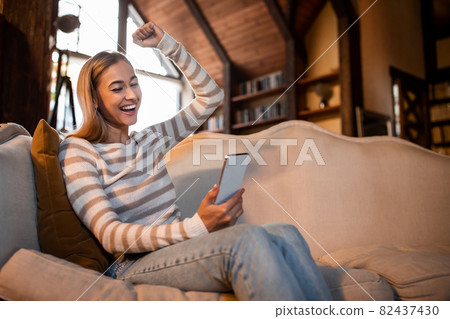 Excited woman using phone shaking clenched fist Excited woman using phone shaking clenched fist 82437430