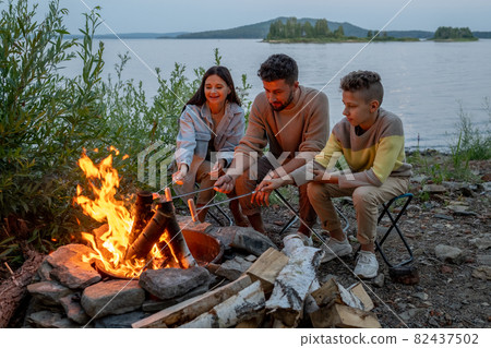 Family of young parents an their son frying sausages Family of young parents an their son frying sausages 82437502