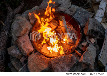 Birch logs burning in campfire surrounded by stones 82437504