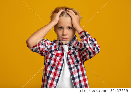 Upset sad surprised caucasian teenage boy presses hands to his head, isolated on yellow background Upset sad surprised caucasian teenage boy presses hands to his head, isolated on yellow background 82437559