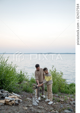 Adolescent boy helping his father to chop firewood Adolescent boy helping his father to chop firewood 82437564