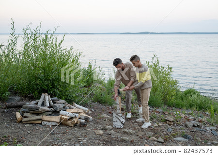 Young man showing his son how to chop firewood Young man showing his son how to chop firewood 82437573