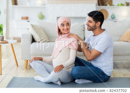 Loving arab husband massaging his pregnant wife, woman feeling relaxed, spouses exercising together on mat 82437702
