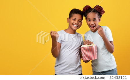 Emotional afro-american siblings watching cartoon together, eating popcorn Emotional afro-american siblings watching cartoon together, eating popcorn 82438121
