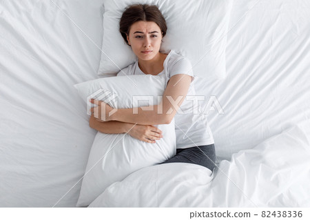 Unhappy sad upset european young woman hugging pillow, suffering from pain and loneliness, lying on bed Unhappy sad upset european young woman hugging pillow, suffering from pain and loneliness, lying on bed 82438336
