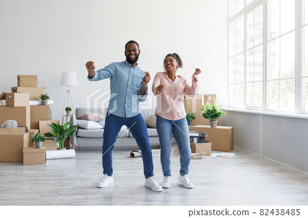 Satisfied young afro american couple dancing in flat with cardboard boxes in home interior, free space 82438485
