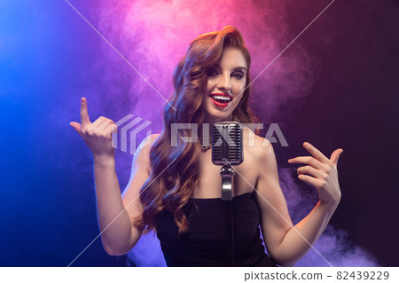 Cropped portrait of beautiful expressive female singer in motion isolated over gradient blue purple background in neon light with stage smoke 82439229