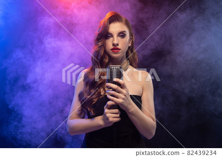 Side view portrait of beautiful femalesinging isolated over gradient blue purple background in neon light with stage smoke Side view portrait of beautiful femalesinging isolated over gradient blue purple background in neon light with stage smoke 82439234