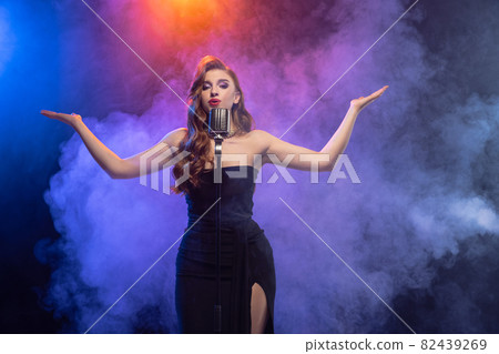 Cropped portrait of young artist, female singer isolated over gradient blue purple background in neon light with stage smoke. 82439269