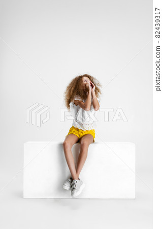 Studio shot of cute curly girl in casual clothes sitting on big box isolated on white background. Studio shot of cute curly girl in casual clothes sitting on big box isolated on white background. 82439317