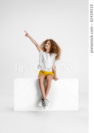 Studio shot of cute curly girl in casual clothes sitting on big box isolated on white background. Studio shot of cute curly girl in casual clothes sitting on big box isolated on white background. 82439318