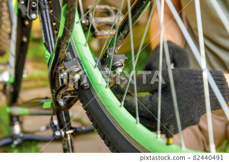 Bike mechanic man repairs bicycle in bicycle repair shop, outdoor. Hand of cyclist bicyclist examines, fixes modern cycle transmission system. Bike maintenance, sport shop concept. Bike mechanic man repairs bicycle in bicycle repair shop, outdoor. Hand of cyclist bicyclist examines, fixes modern cycle transmission system. Bike maintenance, sport shop concept. 82440491
