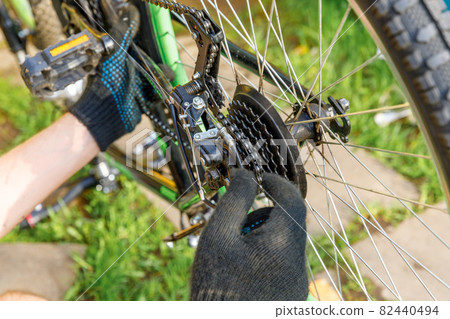 Bike mechanic man repairs bicycle in bicycle repair shop, outdoor. Hand of cyclist bicyclist examines, fixes modern cycle transmission system. Bike maintenance, sport shop concept. Bike mechanic man repairs bicycle in bicycle repair shop, outdoor. Hand of cyclist bicyclist examines, fixes modern cycle transmission system. Bike maintenance, sport shop concept. 82440494