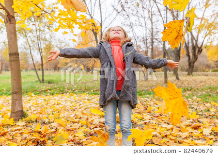 Happy young girl playing under falling yellow leaves in beautiful autumn park on nature walks outdoors. Little child throws up autumn orange maple leaves. Happy young girl playing under falling yellow leaves in beautiful autumn park on nature walks outdoors. Little child throws up autumn orange maple leaves. 82440679