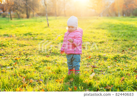 Happy young girl smiling in beautiful autumn park on nature walks outdoors. Little child playing with falling yellow maple leaf in autumn fall orange yellow background. Hello autumn concept. Happy young girl smiling in beautiful autumn park on nature walks outdoors. Little child playing with falling yellow maple leaf in autumn fall orange yellow background. Hello autumn concept. 82440683