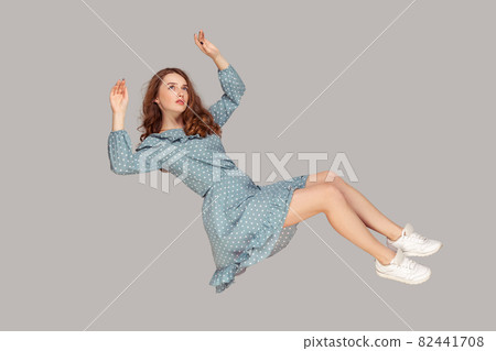 Hovering in air. Full length beautiful pensive girl in vintage ruffle dress levitating flying in mid-air, looking up 82441708