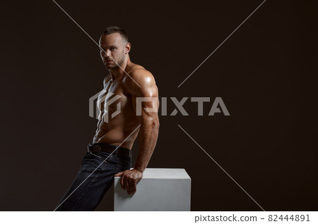 Male muscular athlete sitting on cube in studio 82444891