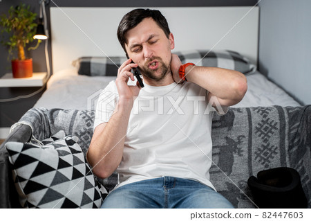 Man in foam cervical collar is calling on phone to the insurance company for medical assistance after accident, feeling neck pain, injury and suffering at home. A male with neck injury calls doctor 82447603