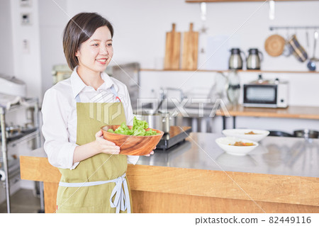 A young woman in an apron serving salad in the kitchen 82449116