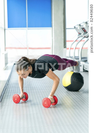 Woman doing floor workout at gym. Fitness girl doing dumbbells and medicine ball plank 82449680