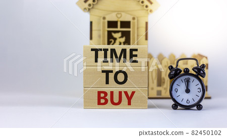 Time to buy real estate. Wooden blocks form the words 'time to buy' near miniature house. Black alarm clock. Beautiful white background. Business concept. Copy space. 82450102