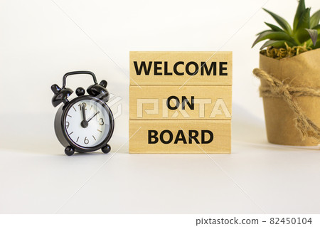 Welcome on board symbol. Wooden blocks with words 'Welcome on board'. Beautiful white background, black alarm clock, house plant. Business, welcome on board concept, copy space. 82450104