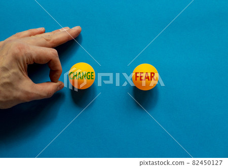 Fear vs change symbol. Male hand is about to flick the ball. Orange table tennis balls with words fear and change. Beautiful blue background. Business, fear vs change concept. 82450127