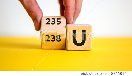 Uranium enrichment symbol. Hand turns the cube and changes the word '238 U' to '235 U'. Beautiful yellow, white background, copy space. Business, nuclear technology and uranium enrichment concept. Uranium enrichment symbol. Hand turns the cube and changes the word '238 U' to '235 U'. Beautiful yellow, white background, copy space. Business, nuclear technology and uranium enrichment concept. 82450143