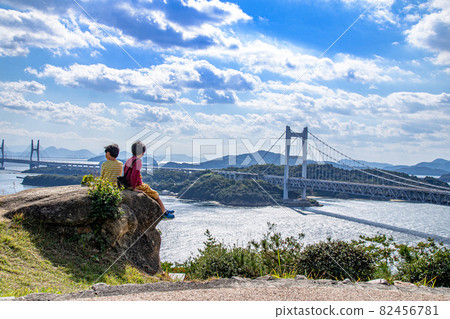 Brothers sitting in harmony and looking at the Seto Ohashi Bridge and the Seto Inland Sea, Kurashiki City, Okayama Prefecture 82456781
