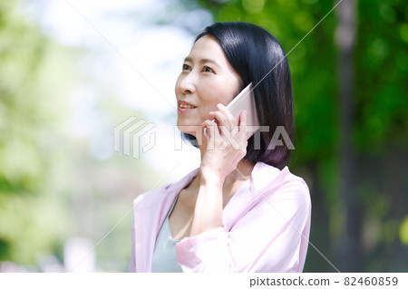 Middle-aged woman wearing sportswear in the fresh green and using a smartphone 82460859