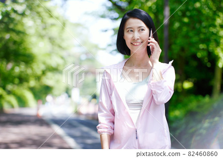 Middle-aged woman wearing sportswear in the fresh green and using a smartphone Middle-aged woman wearing sportswear in the fresh green and using a smartphone 82460860