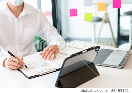 Two colleagues wearing surgical masks analyzing the data in chart for marketing research 82465591
