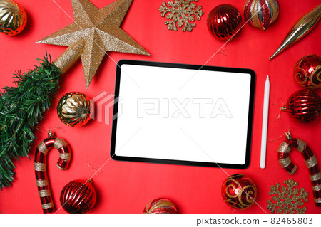 Mock up digital tablet, gold ornaments and fir tree branches on red background. Christmas and New year concept. Mock up digital tablet, gold ornaments and fir tree branches on red background. Christmas and New year concept. 82465803