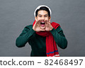 Cheerful young Asian man wearing Christmas attire shouting with hands cupping around mouth in gray  82468497