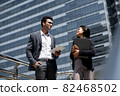 Handsome young Indian businessman in corporate wear talking with businesswoman outdoors in the city 82468502