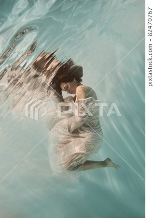 A girl in a blue dress swims underwater on a light background as if in weightlessness A girl in a blue dress swims underwater on a light background as if in weightlessness 82470767