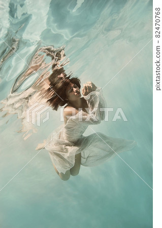 A girl in a blue dress swims underwater on a light background as if in weightlessness A girl in a blue dress swims underwater on a light background as if in weightlessness 82470768