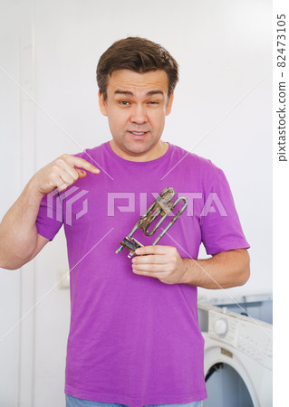 repairman of washing machine holds old tubular electric heater  82473105