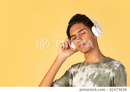 Portrait of young handsome boy, student in casual clothes listening to music isolated on yellow studio backgroud. Human emotions concept. Portrait of young handsome boy, student in casual clothes listening to music isolated on yellow studio backgroud. Human emotions concept. 82473636
