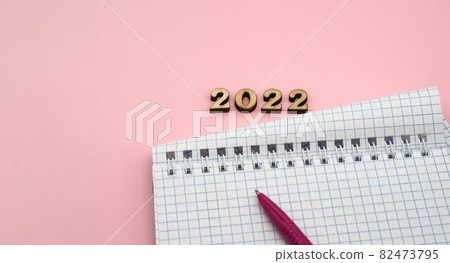Notepad and Pen on Pink. Wooden numbers 2022. Notepad on a spring. Pink Pen. Spiral spiral checkered sheets. 82473795