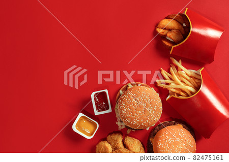 Fast food dish top view. Meat burger, potato chips and nuggets on red background. Takeaway composition. Fast food dish top view. Meat burger, potato chips and nuggets on red background. Takeaway composition. 82475161
