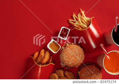 Two hamburgers and french fries, sauces and drinks on red background. Fast food. Top view, flat lay with copyspace 82475174