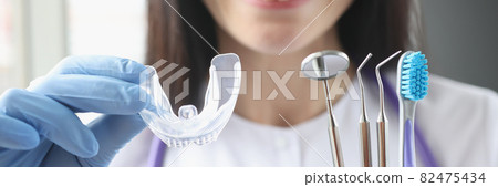 Smiling female doctor holds transparent plastic mouth guard and stomatological instruments in her hand 82475434