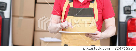 Cute caucasian postman in suit and cap checks mailboxes with tablet device in his hands Cute caucasian postman in suit and cap checks mailboxes with tablet device in his hands 82475559