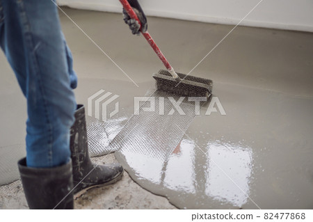 plasterer during floor covering works with self-levelling cement mortar, uses a needle roller plasterer during floor covering works with self-levelling cement mortar, uses a needle roller 82477868