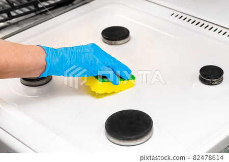 Woman's hand in a household glove sponges a gas stove. Cleaning the kitchen and washing the burners 82478614