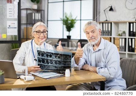 Mature doctor and patient sitting at cabinet with x ray scan Mature doctor and patient sitting at cabinet with x ray scan 82480770