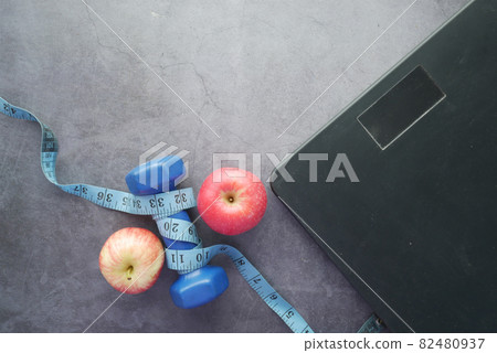 Fitness concept with dumbbell, apple and weight scale on black Fitness concept with dumbbell, apple and weight scale on black 82480937