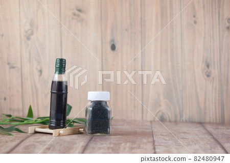 Black Cumin in a container with oil in a jar on table. 82480947